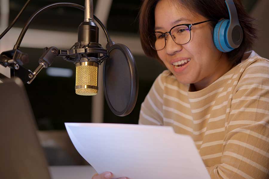 Asian woman doing voice over on microphone reading notes
