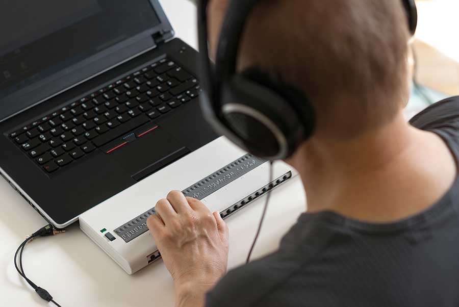 Man on keyboard reading computer text with a braille reader