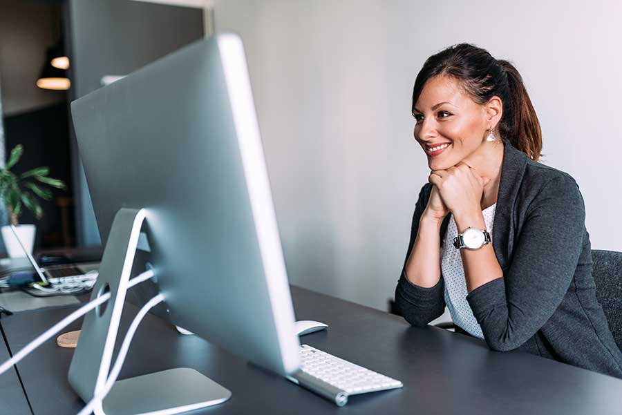AdobeStock_210040473 Femme heureuse lisant des sous-titres à l’écran au bureau