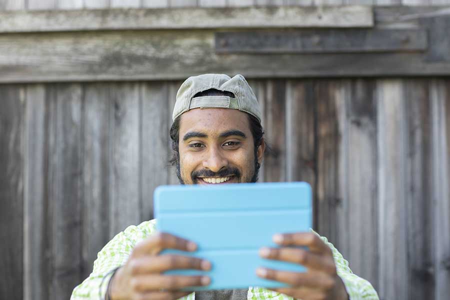 AdobeStock_360954513 Homme indien sur un iPad souriant