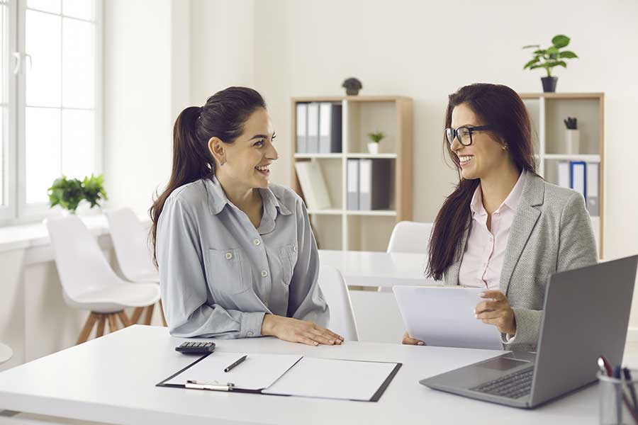 AdobeStock_416501914 Two women having a friendly discussion at an office