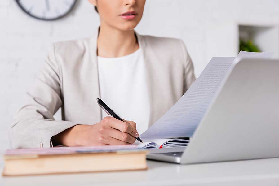 Femme écrivant avec un stylo à un bureau avec un ordinateur portable.