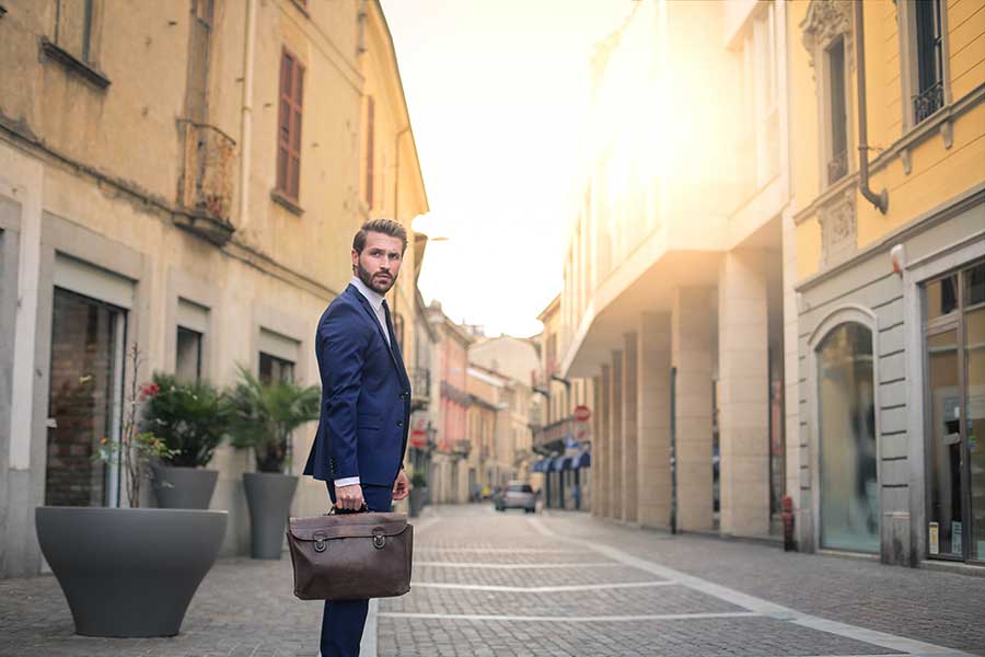 Homme italien en costume avec porte-documents debout dans une rue de la vieille ville italienne.