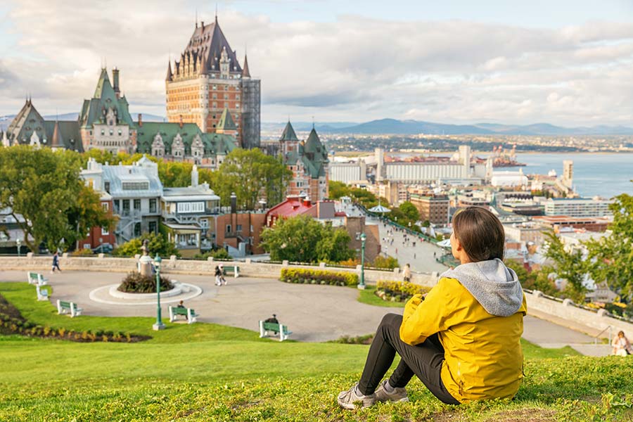 Woman with her back turned sitting on a hill looking at Quebec City