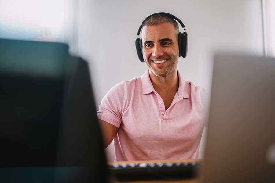 Man on headphones looking as desktop computer screens.