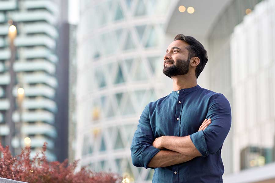 Positive man with folded arms looking upwards in a city setting. 