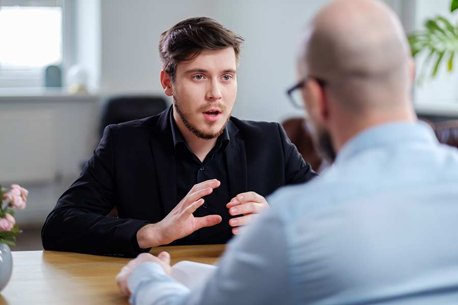 Young man in a meeting with an older man gesturing with his hands. 
